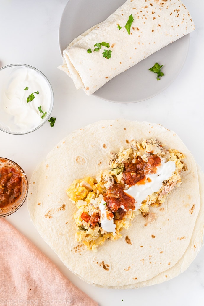 slow cooker breakfast burritos on a plate with salsa and sour cream