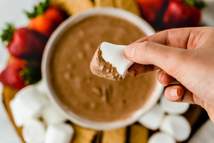 hand holding marshmallow dipped in smores dip