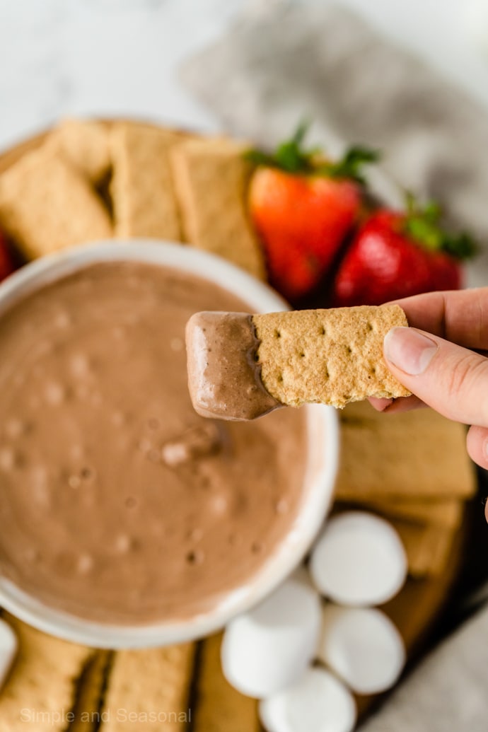 hand holding graham cracker dipped in chocolate s'mores dip