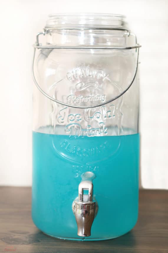 clear drink dispenser filled halfway with blue punch