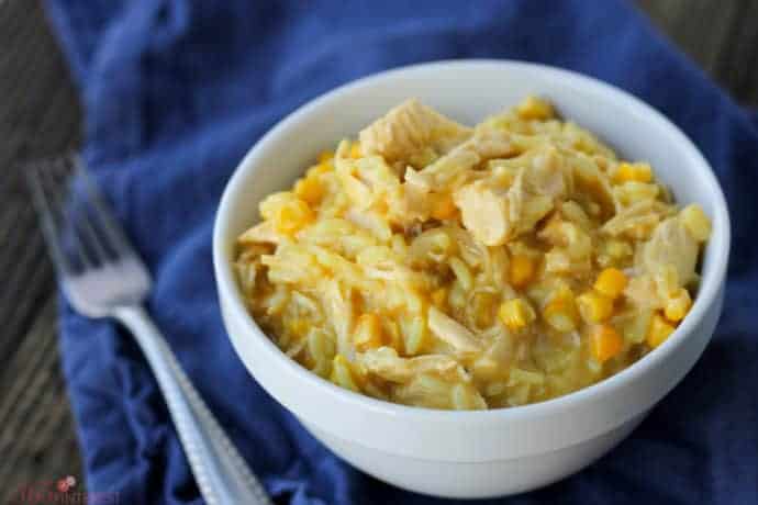 white bowl with cooked chicken and rice with corn on a blue napkin