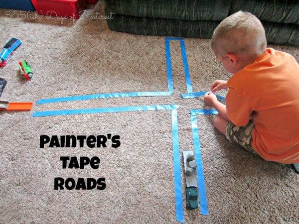 young boy placing blue painters tape on the carpet to make roads