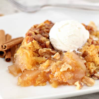 cooked apple cinnamon dump cake topped with ice cream on a white plate