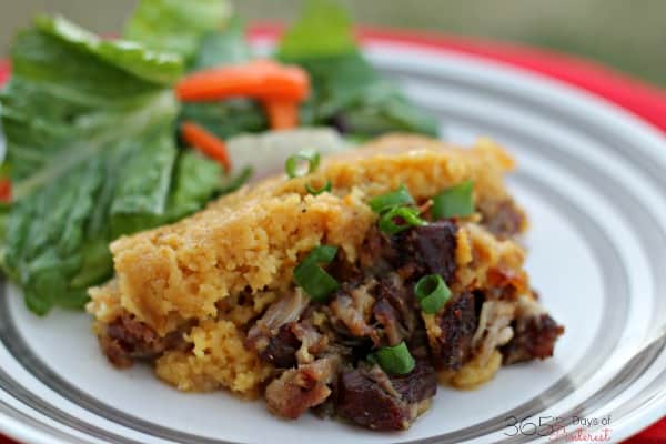 Cooked pork shoulder and tamale cornbread topping on a plate with red napkin in the background