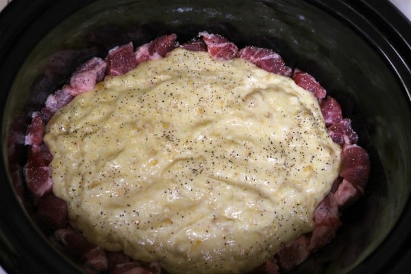 raw pork shoulder pieces with corn bread mixture in the center pictured inside the Crockpot