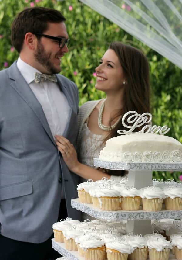 couple standing behind tower of wedding themed cupcakes