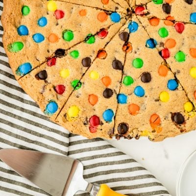 Giant Cookie Cake sliced like pizza with serving spatula and striped towel