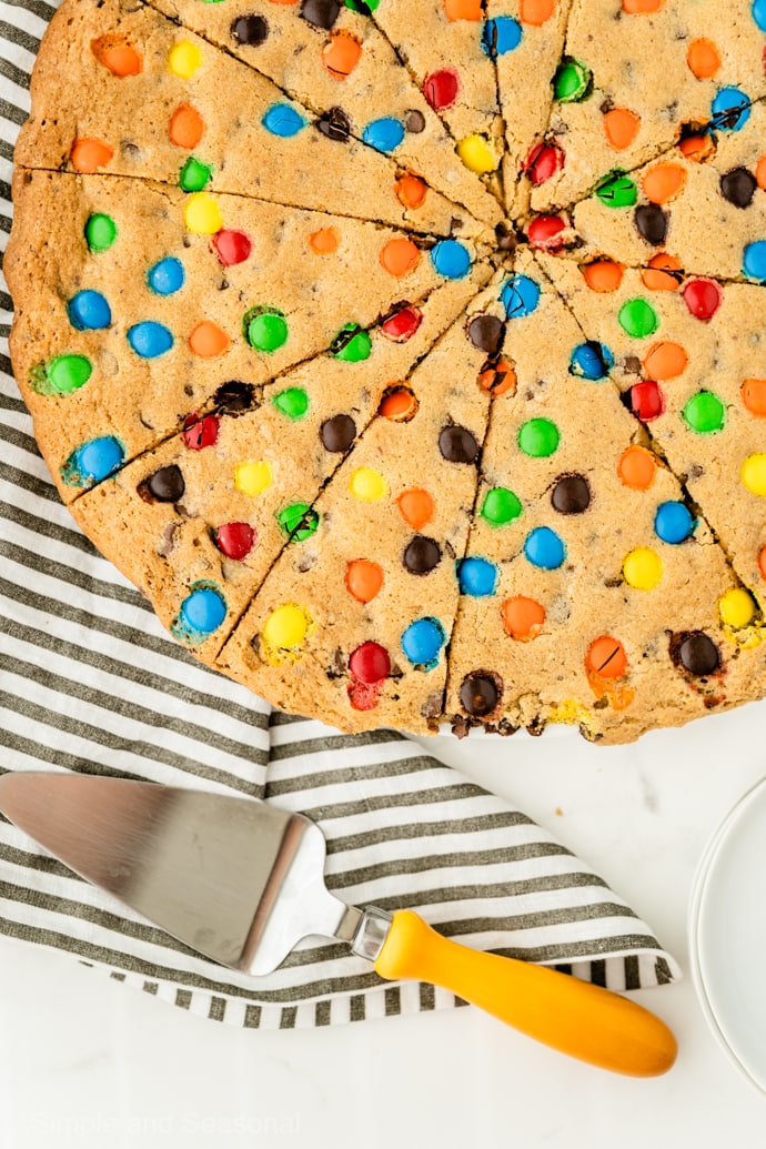 Giant Cookie Cake sliced like pizza with serving spatula and striped towel