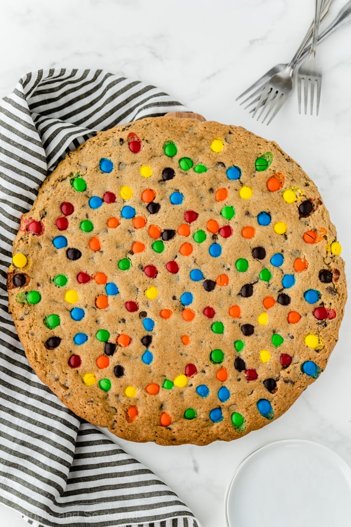 baked, golden brown giant cookie cake with striped kitchen towel in background