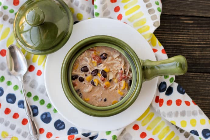 soup with corn, black beans and tomatoes in a green handled crock