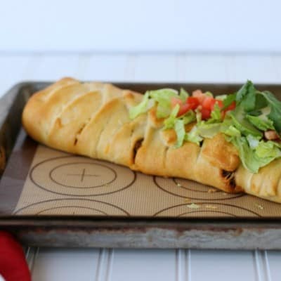 whole cooked taco braid on a sheet pan, topped with lettuce and tomatoes