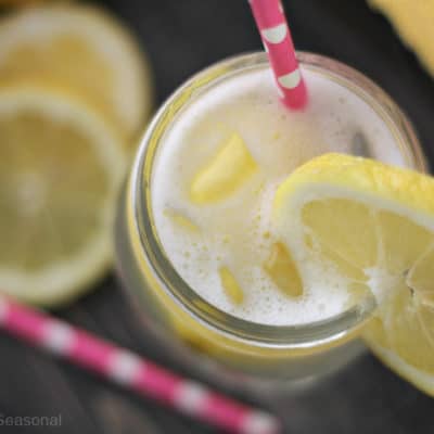 bubbly lemon drink in jar with fresh lemons and pink straw on dark background