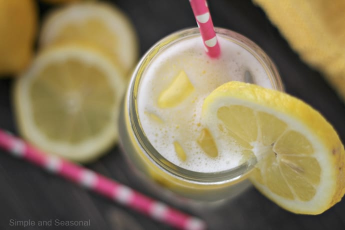 bubbly lemon drink in jar with fresh lemons and pink straw on dark background