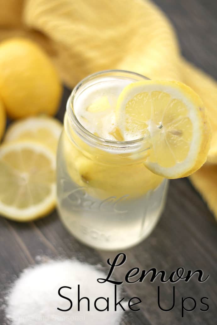 jar of lemon drink with lemon slices and pile of sugar in background; text label reads Lemon Shake Ups