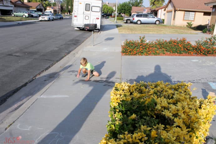 young boy tracing brother's long shadow with sidewalk chalk