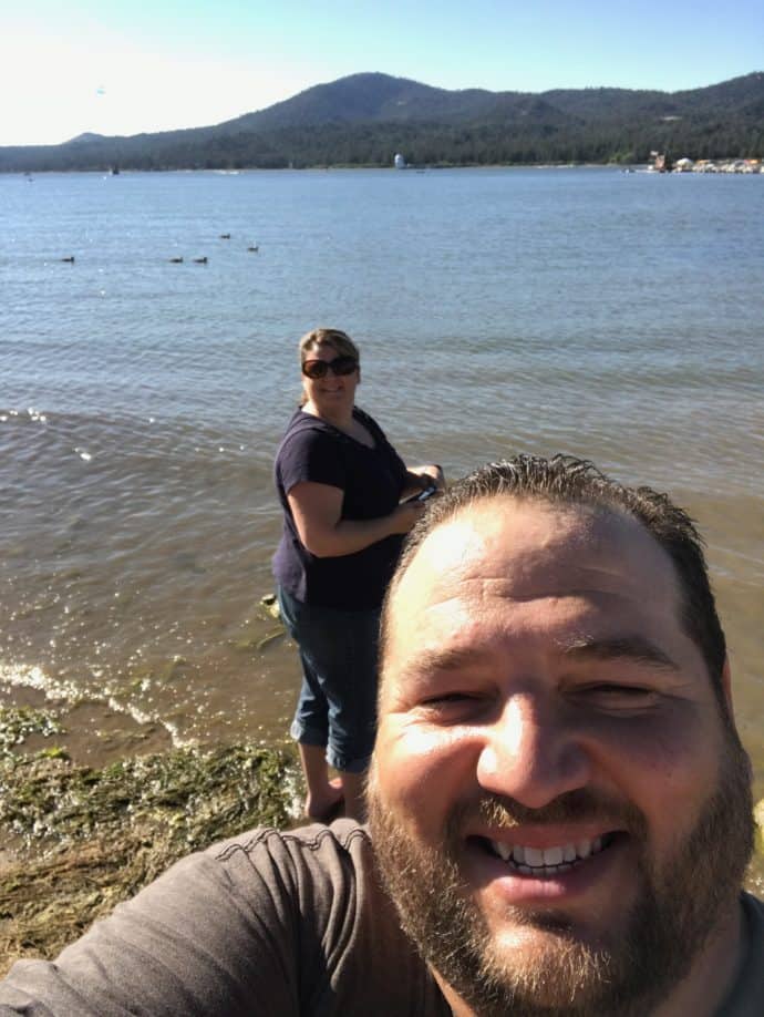 man and woman at the side of a lake with mountains in the background