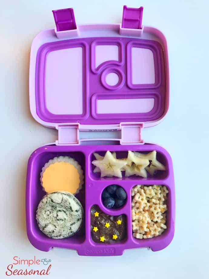 vertical: sandwich decorated like sun and moon, star puffs, apple slices and other snacks in lunchbox 