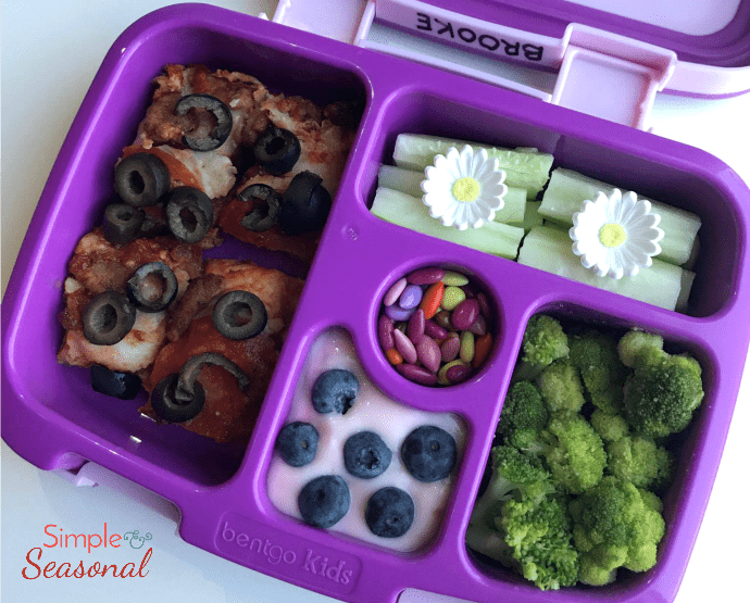 pizza, yogurt with berries, zucchini, broccoli and small candies in bento box