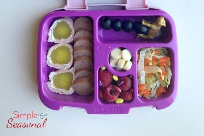 pickle rolls, sausage, salad, string cheese, olives and berries in bento box