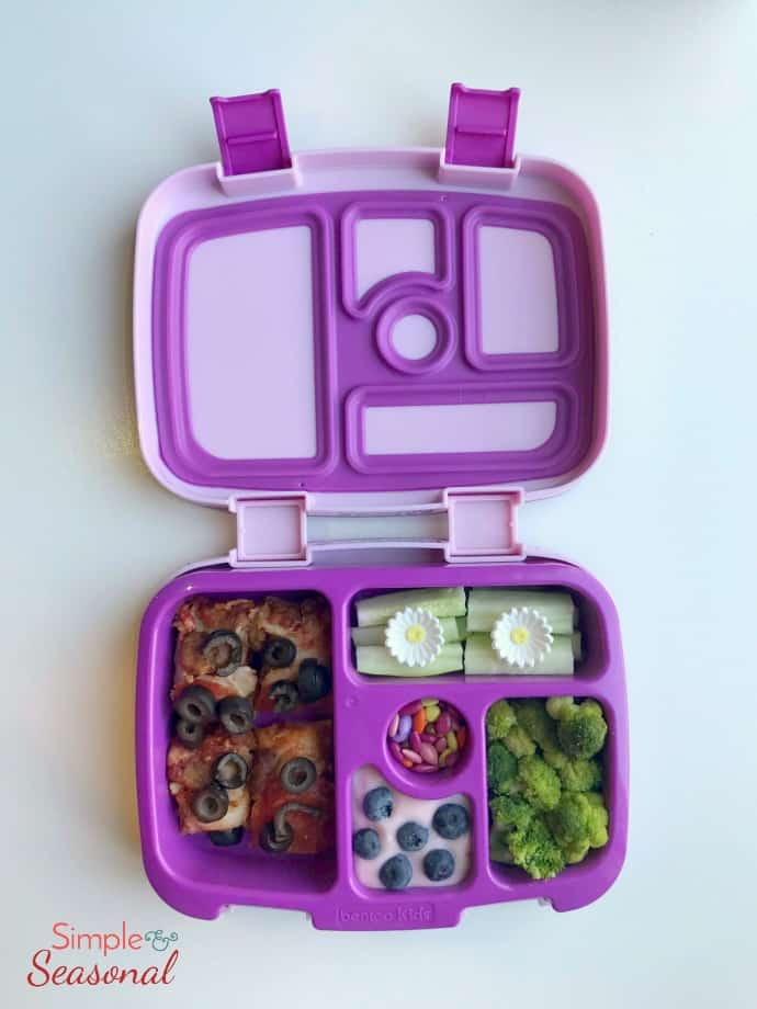 pizza, yogurt with berries, zucchini, broccoli and small candies in bento box