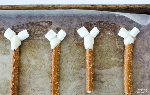 top down view of pretzel rods dipped in melting candy and mini marshmallows attached to the top