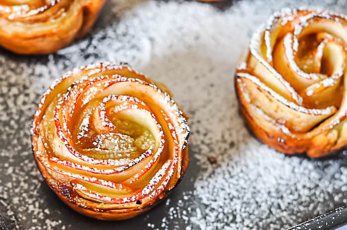 apple pastries shaped like roses on plate dusted with powdered sugar