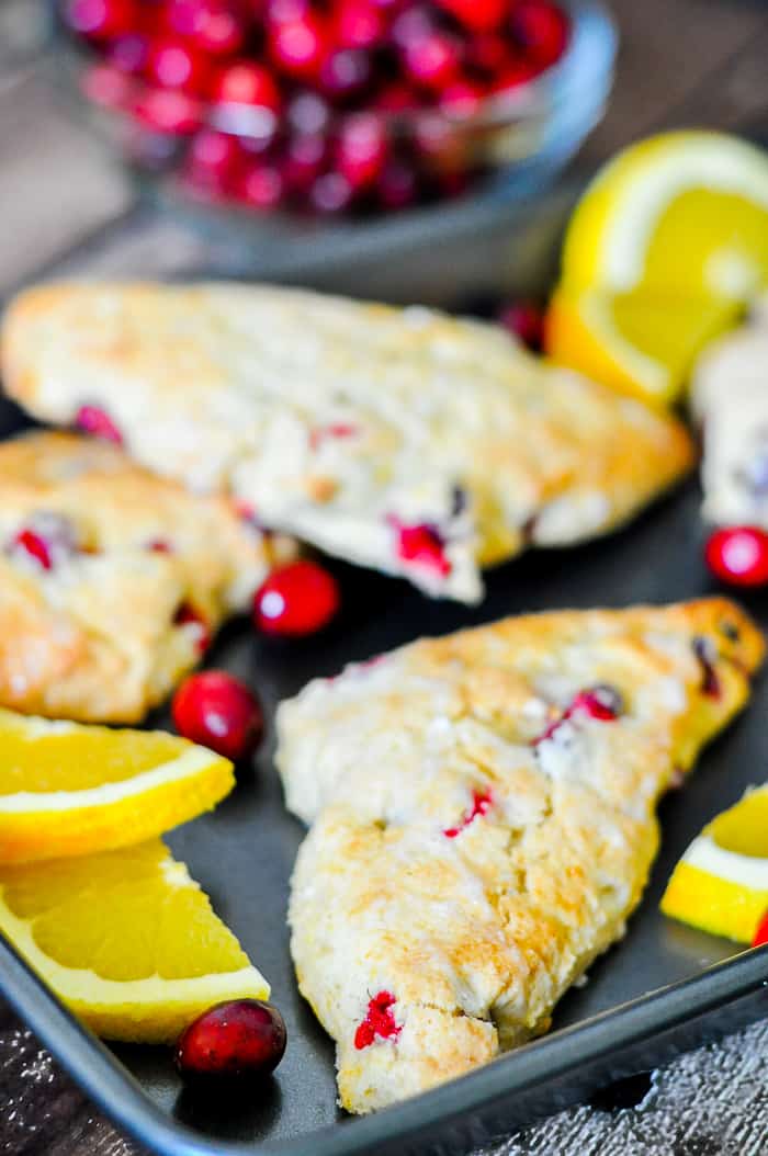 orange scones with chunks of red cranberries on baking sheet
