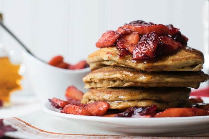 Stack of pancakes on a plate covered with apples and cranberry in syrup