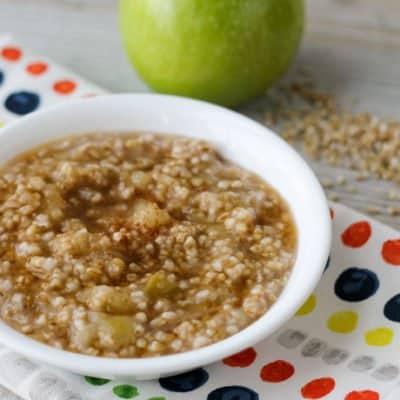 bowl of cooked oatmeal with apple in background