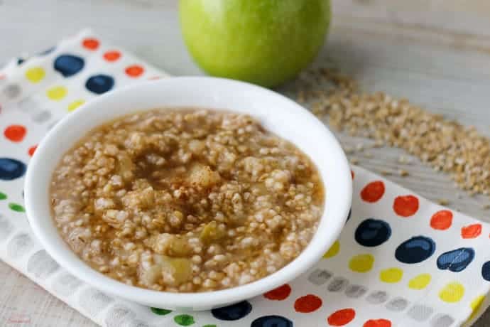 bowl of cooked oatmeal with apple in background