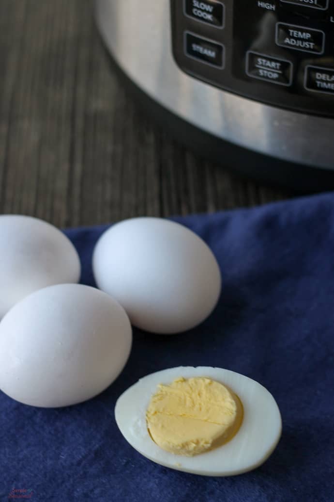 vertical image of 3 hard boiled eggs in shell with one sliced open to show insides