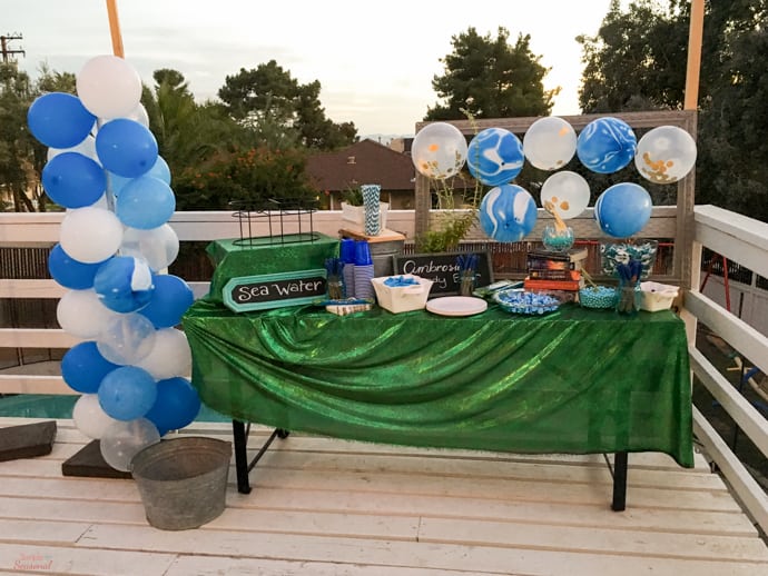drink and candy table decorated with blue and white balloons and green tablecloth