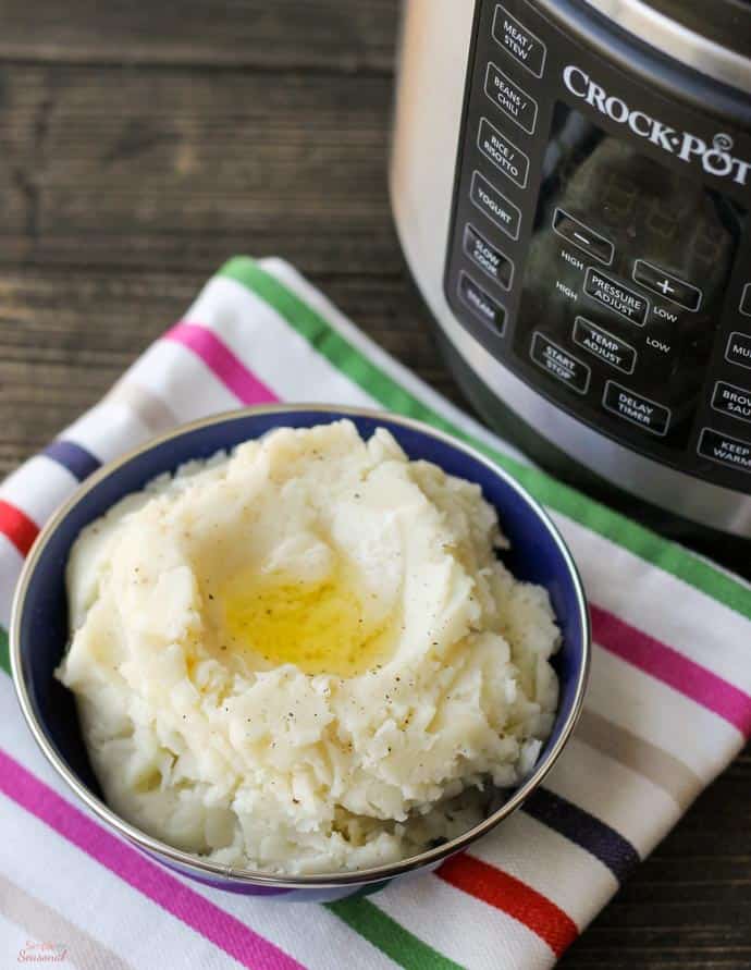 mashed potatoes in a bowl with melted butter with pressure cooker in the background