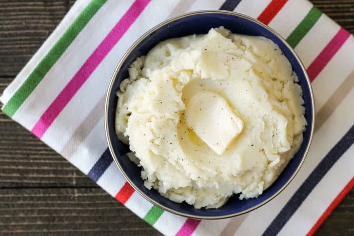 top down view of bowl of mashed potatoes topped with butter and salt and pepper