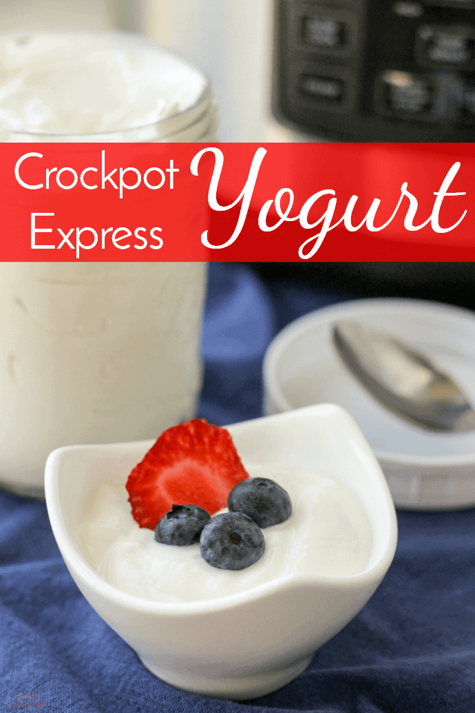 small white bowl of yogurt topped with strawberry slice and 3 blueberries and larger jar in the background; text label reads Crockpot Express Yogurt