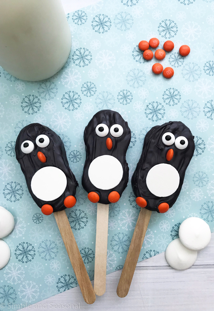 3 decorated penguin nutter butter cookies on a stick with glass of milk