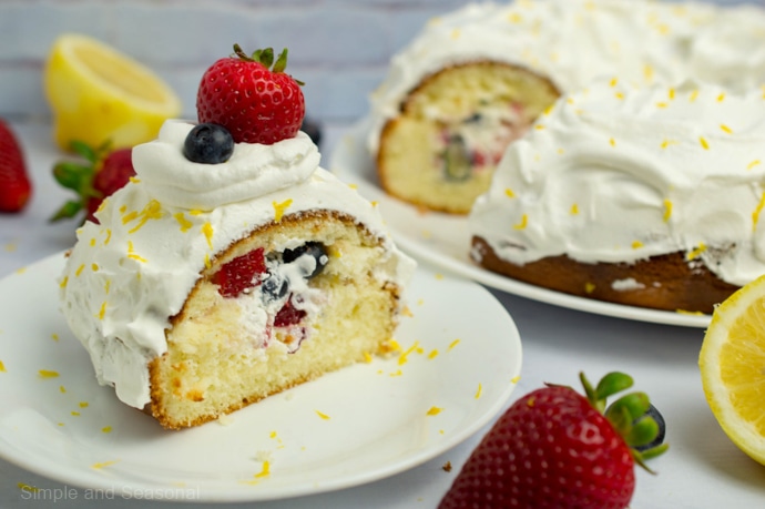 Slice of lemon bundt cake on a white plate topped with berries and showing cream and berries inside