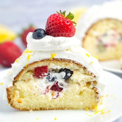 close up of slice of lemon bundt cake stuffed with berries and cream and topped with strawberry