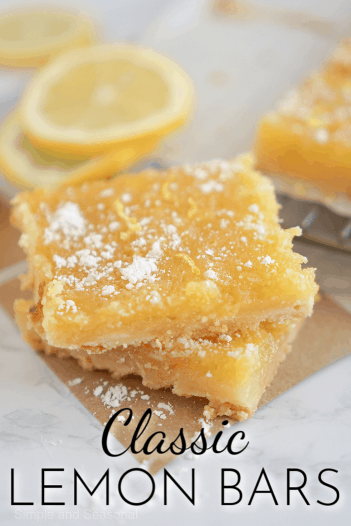 two stacked lemon bars on a napkin with lemon slices in the background
