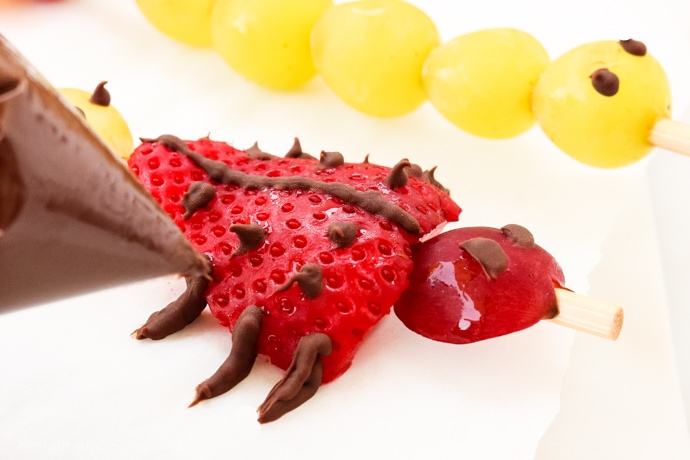 piping chocolate onto strawberry to look like legs