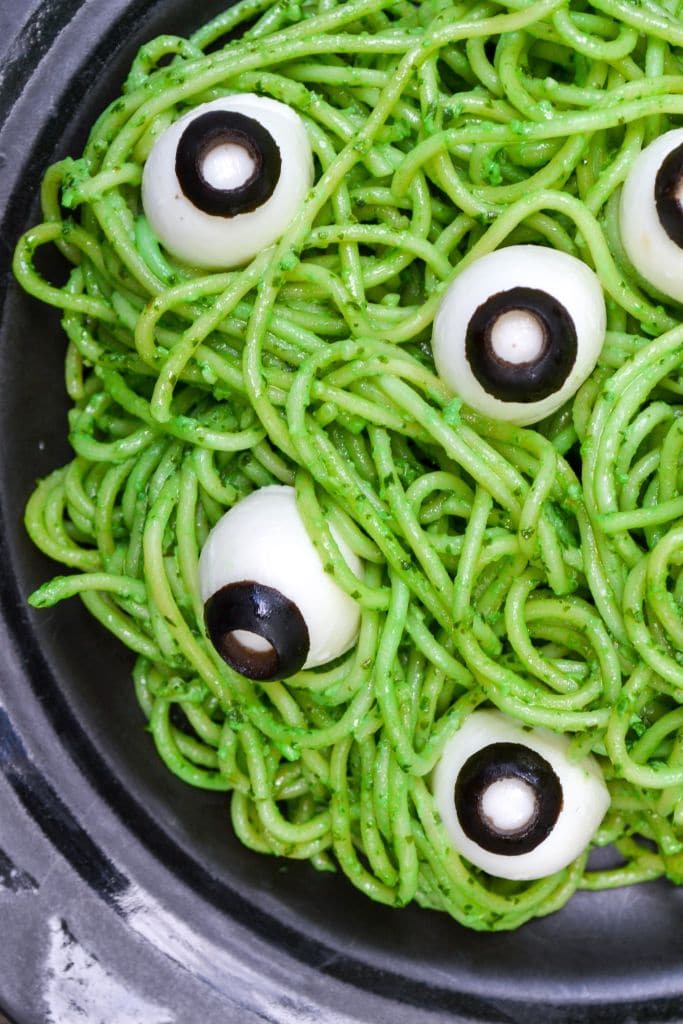 green colored stringy pasta topped with eggs and olives to look like eyes