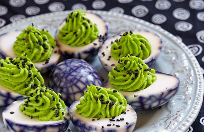 dyed deviled eggs with green filling on a plate with black and white decorations