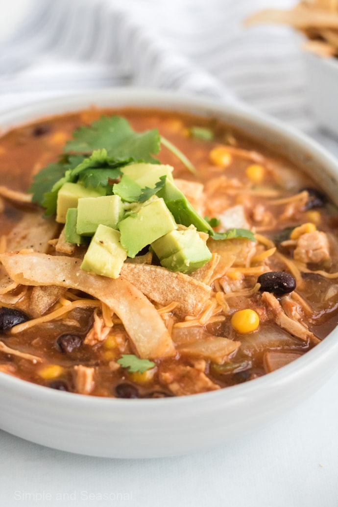 bowl of chicken tortillas soup topped with fresh avocado pieces and crispy tortilla strips