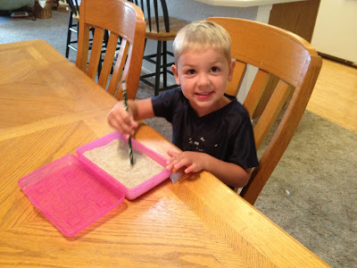 young boy writing in the sand with a pencil