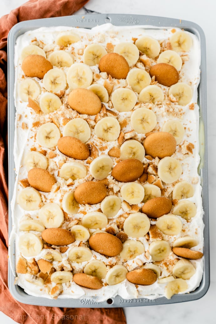 Banana pudding poke cake covered with whipped topping, banana slices and wafer cookies