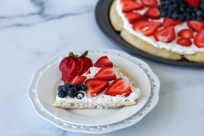 slice of fruit pizza on a plate with the pizza pan in the background