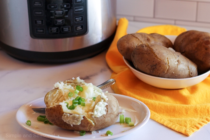 cooked potato on plate with 3 cooked potatoes in a large bowl