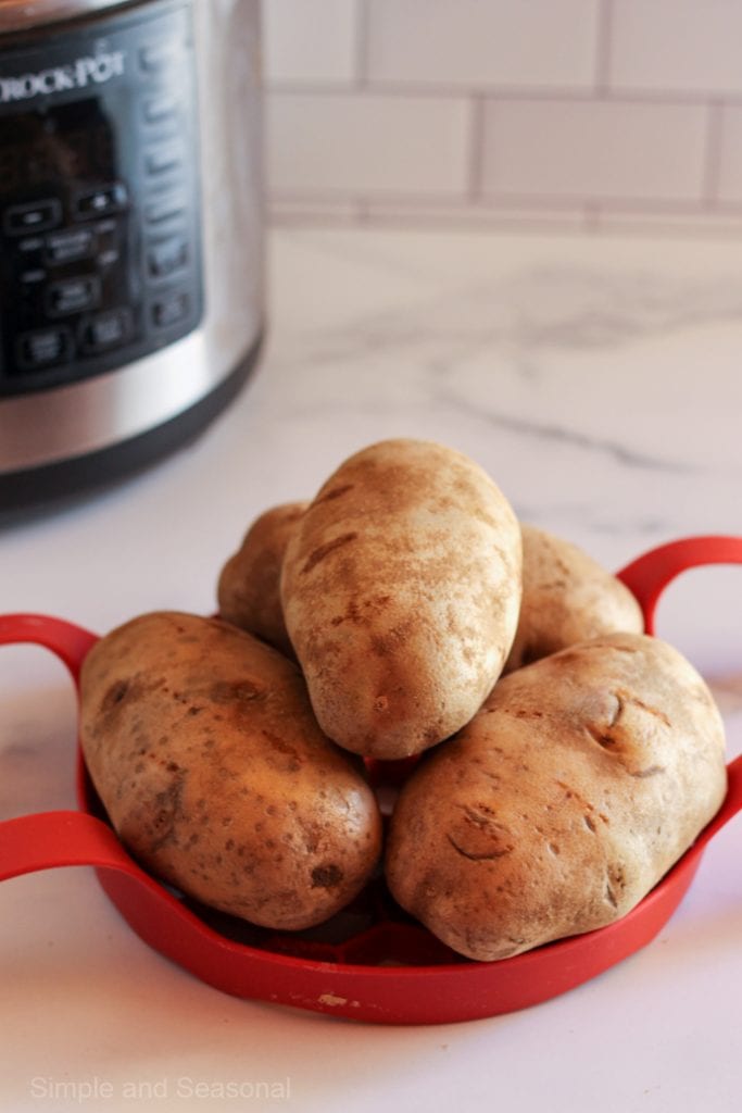 four raw potatoes stacked up on a red trivet