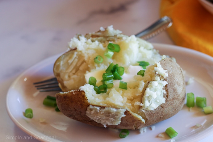cooked potato on plate with sour cream and butter