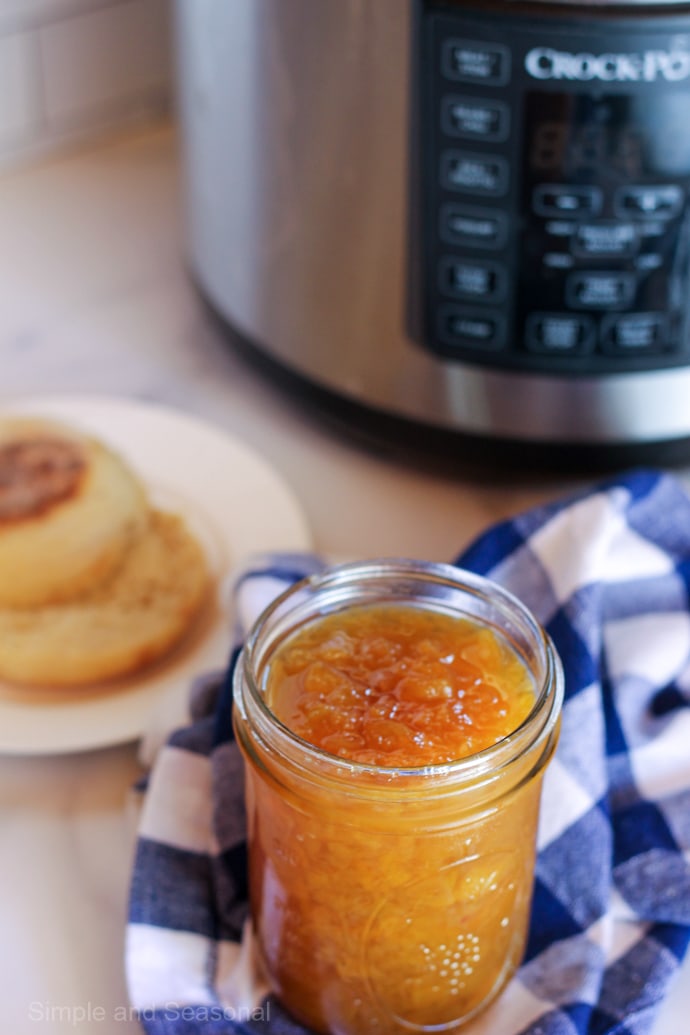 jar of peach jam on blue and white checked napkin with Crockpot Express in background